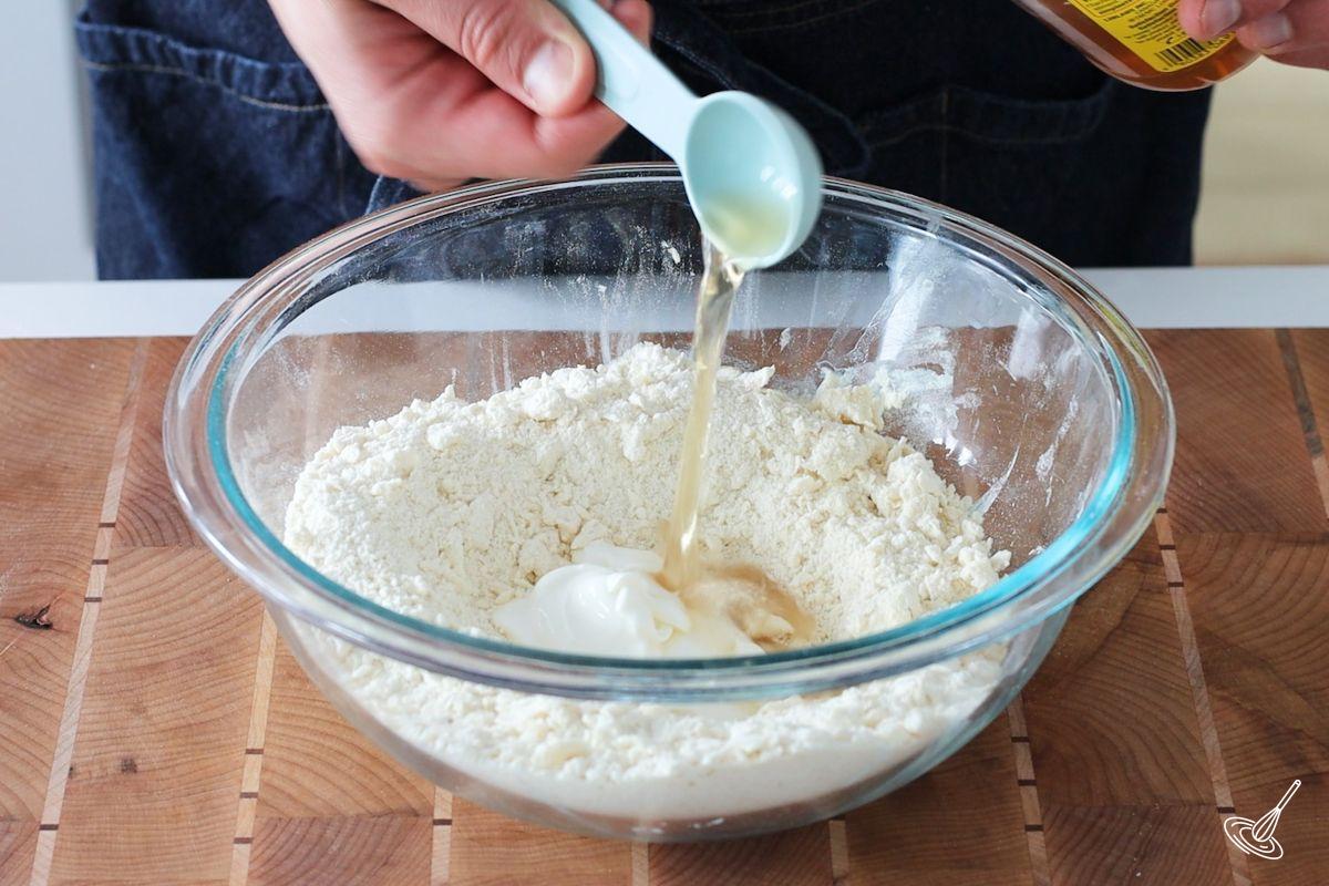 Someone adding vinegar to a bowl of flour.