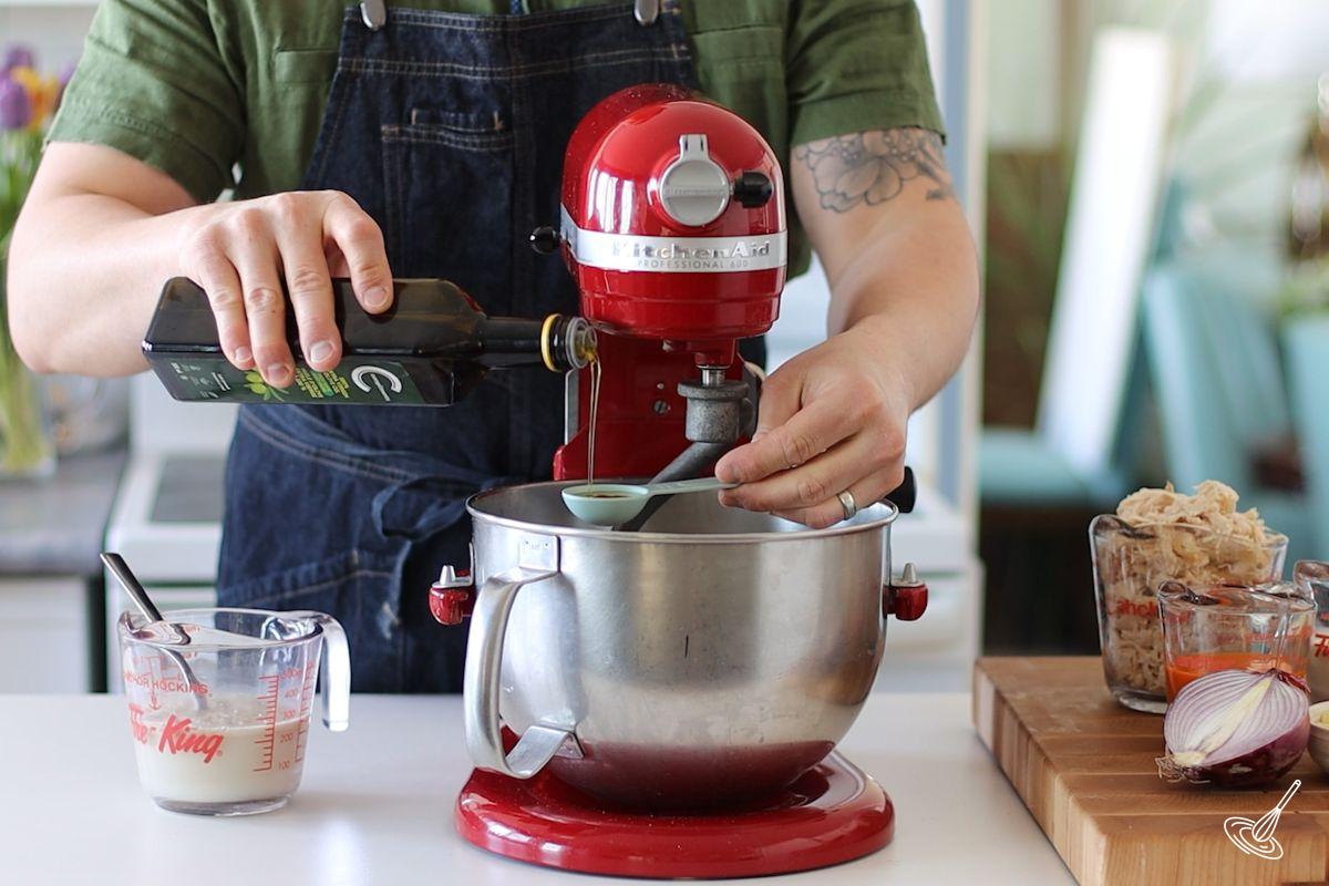 Someone adding olive oil to the bowl of a stand mixer. 