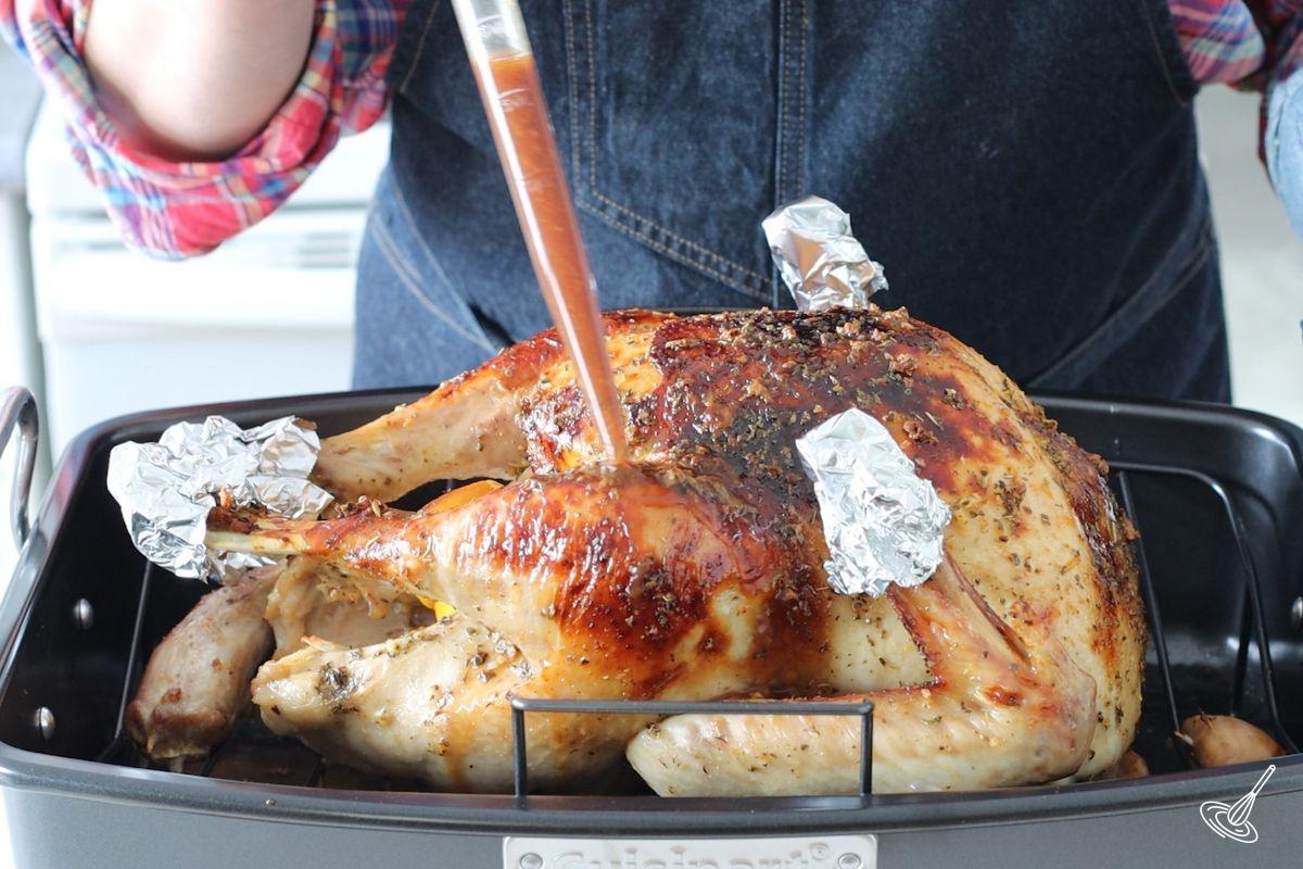 Someone using a baster to glaze the turkey roast.