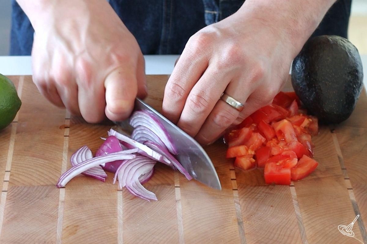 Someone cutting thin sliced of red onion. 