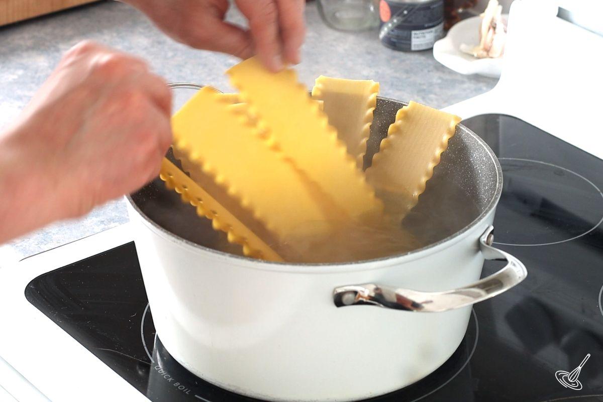 Someone adding lasagna noodles to a large pot of boiling water.