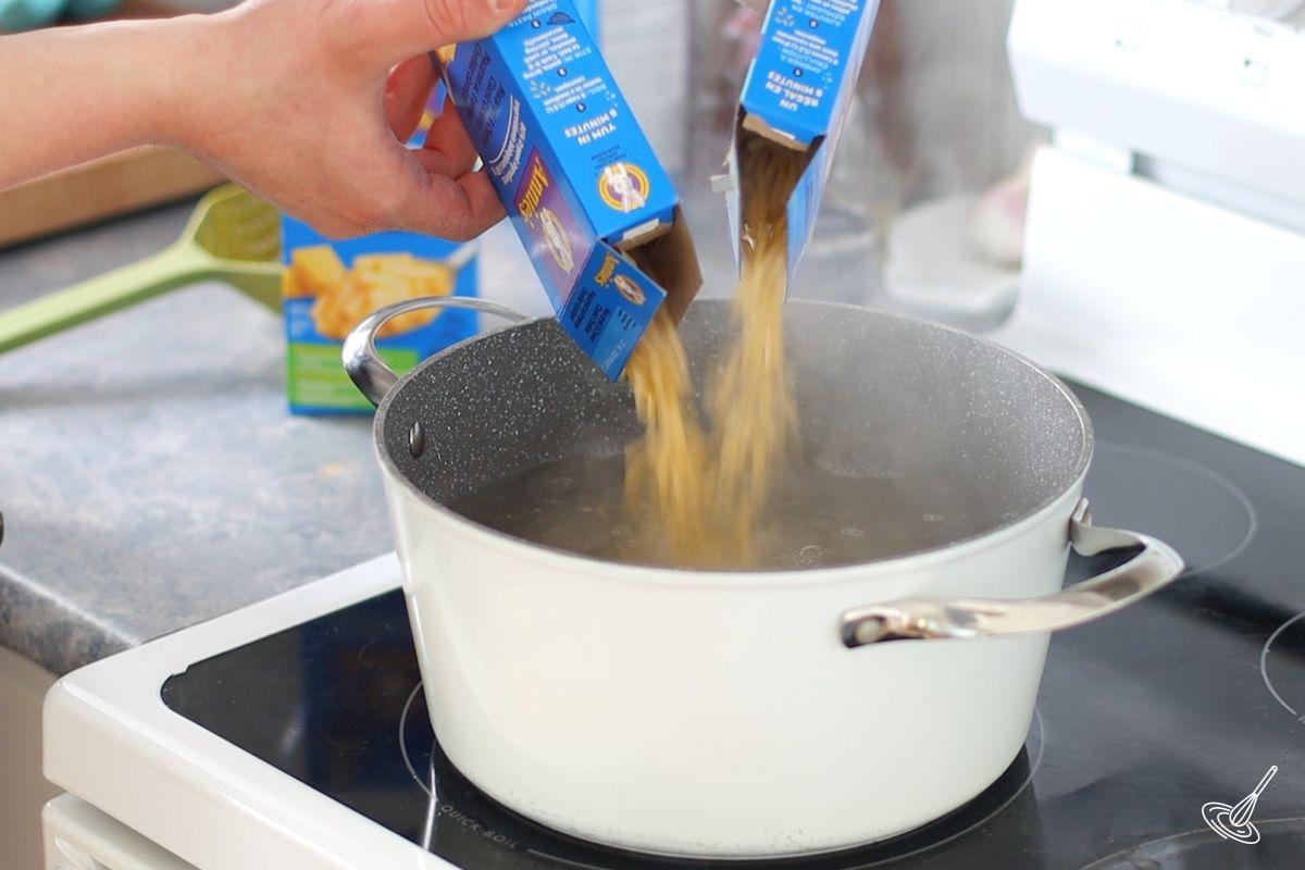Someone adding macaroni noodles to a large pot of boiling water. 