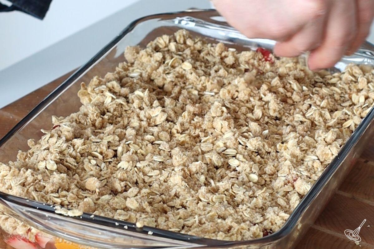 Someone sprinkling oat crumble on top of fruit in a baking dish.