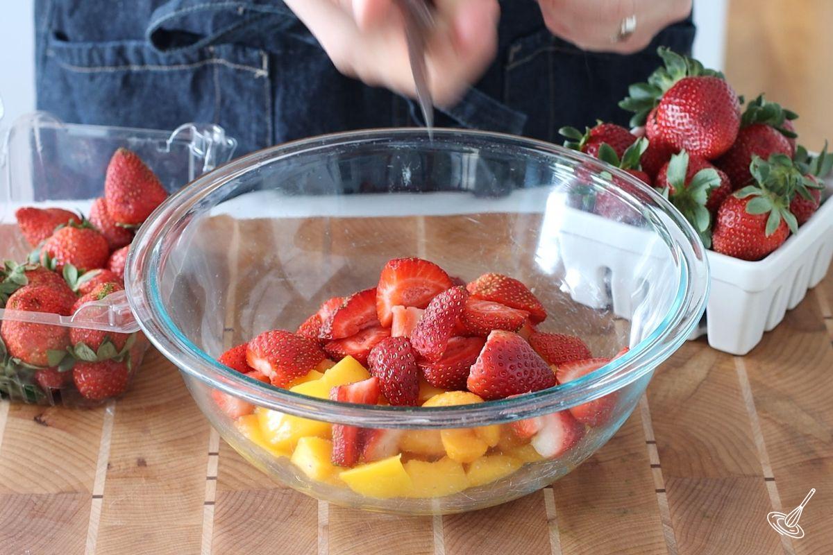 Quelqu'un coupe des fraises et des pêches dans un grand bol.