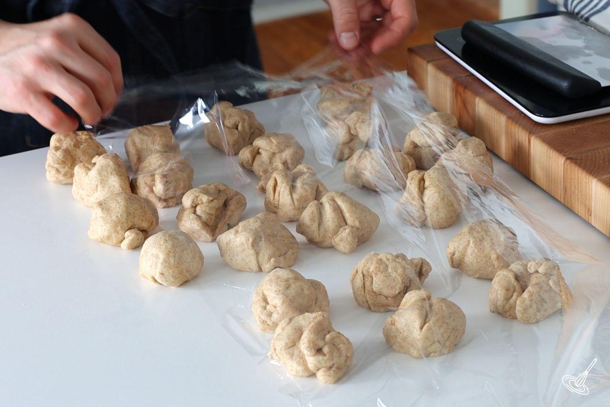 Someone covering portioned honey whole wheat dinner rolls dough with plastic wrap.