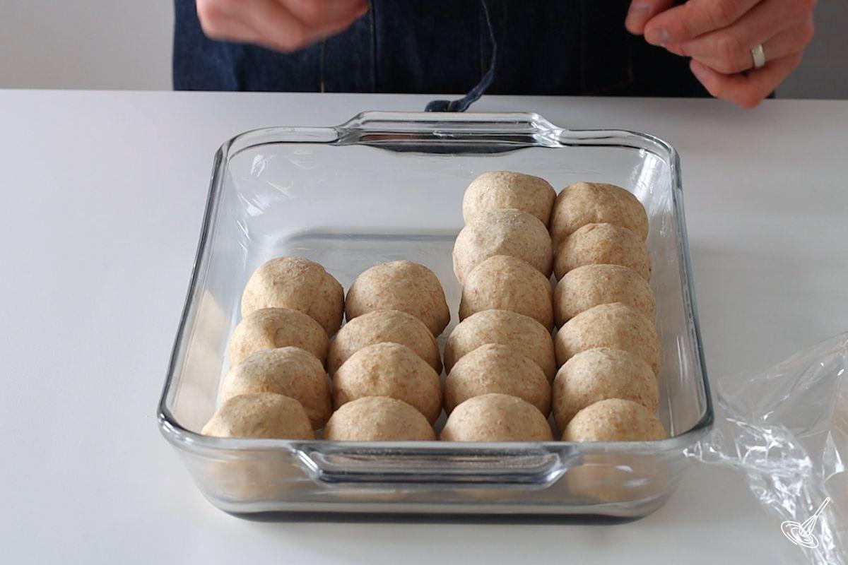 Someone placing balls of honey whole wheat dough in a baking dish. 