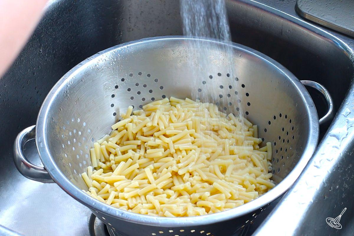 Cooked macaroni noodles in a stainless steel strainer.