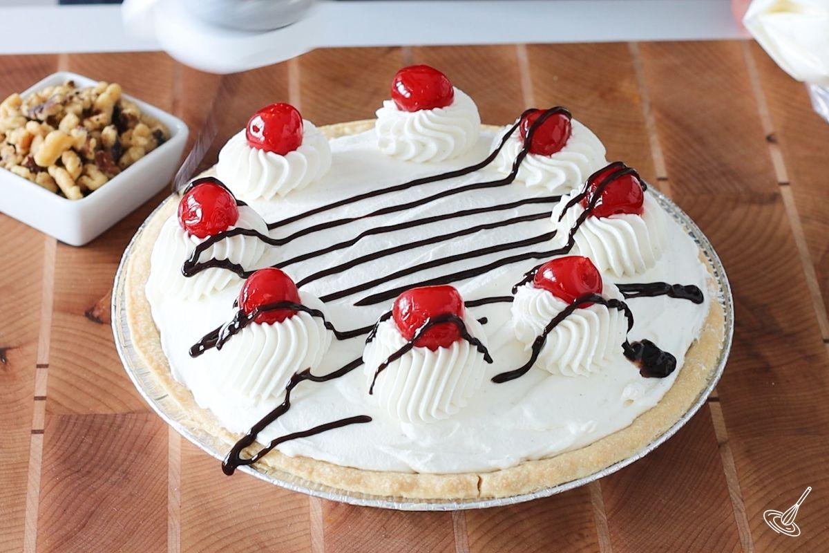 Someone drizzling chocolate sauce over a cream pie. 