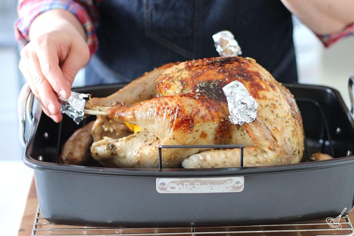 Someone adding foil covers on the turkey wing tips and legs. 