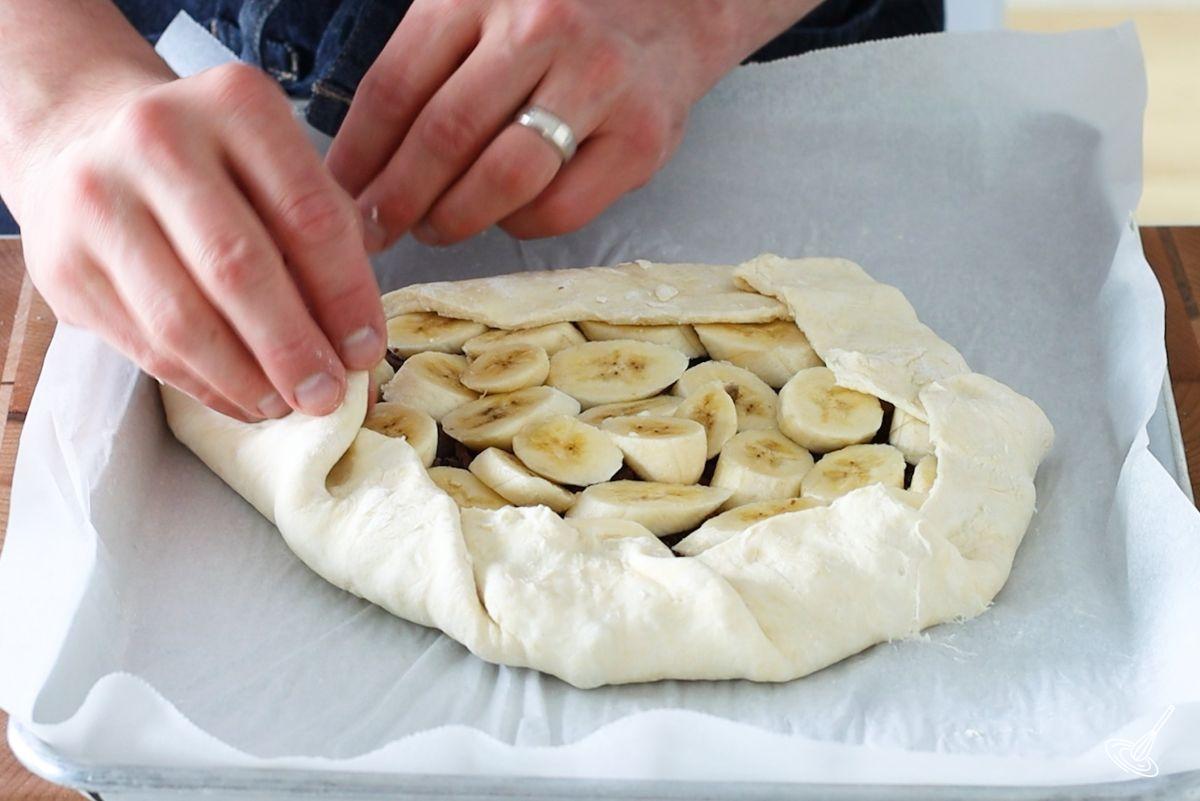 Someone folding edges of dough over filling of banana chocolate galette.