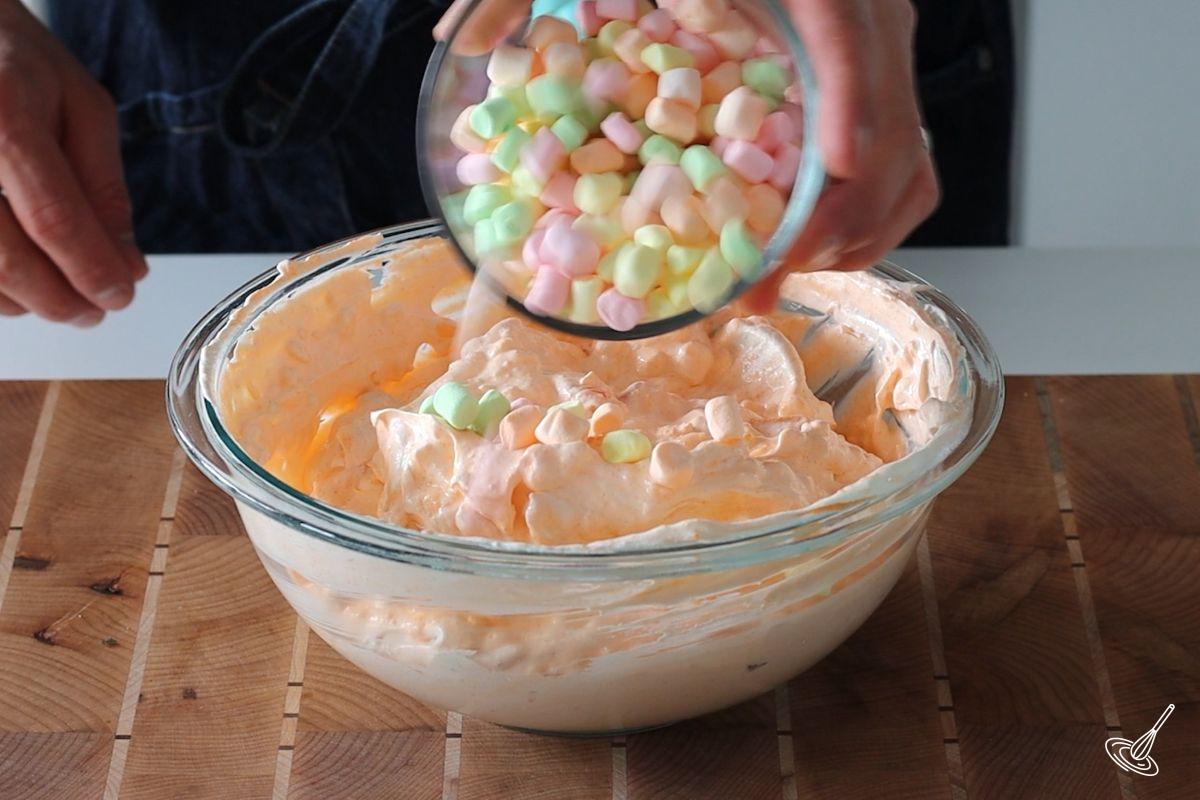 Someone adding mini marshmallows to the Orange Jello Cottage Cheese Salad.