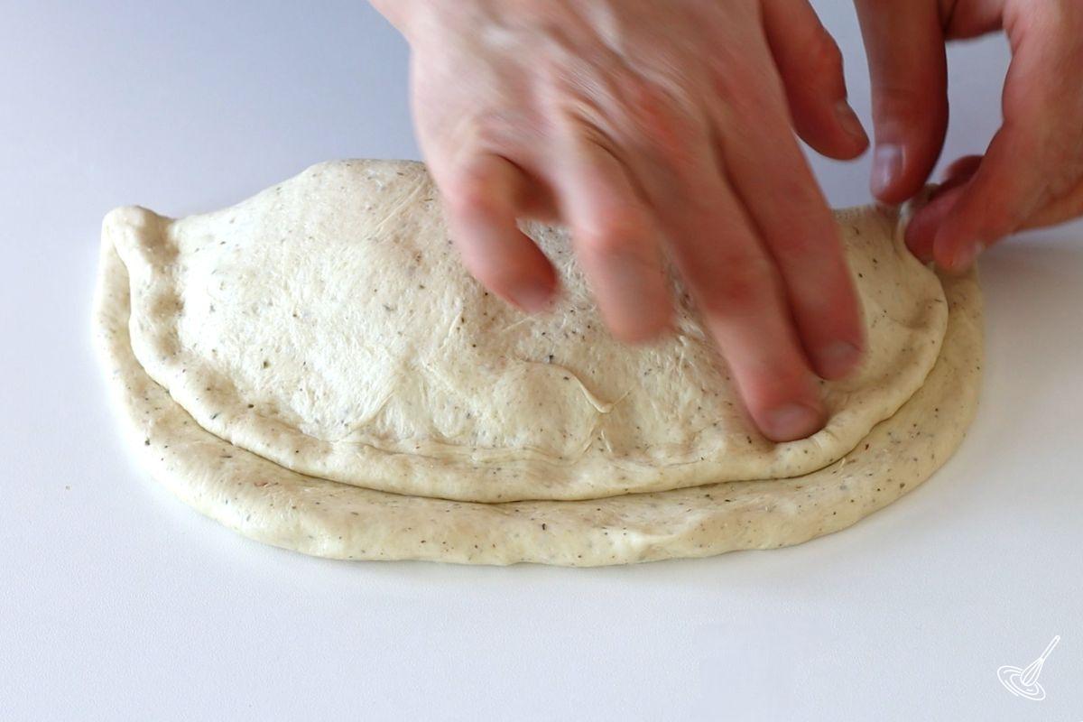 Someone pressing down on the dough of a closed calzone. 