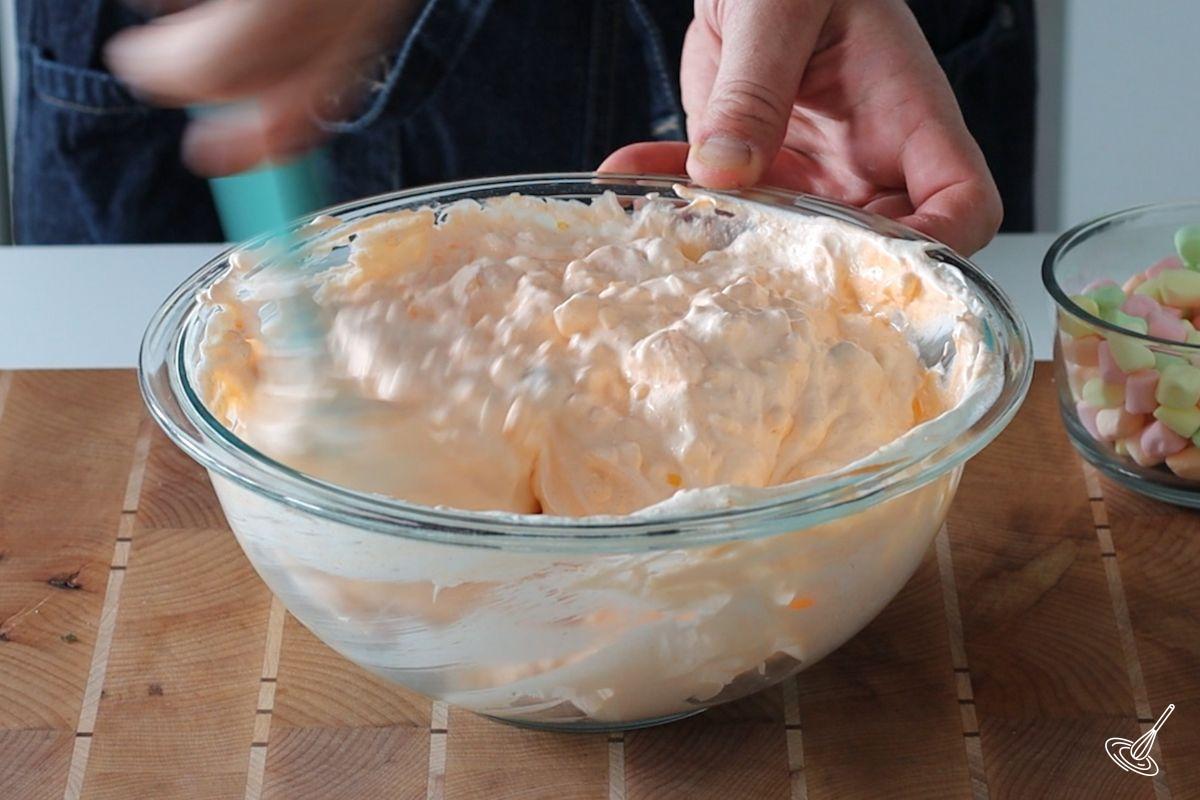 Someone folding whipped topping in a large bowl of orange cottage cheese salad.