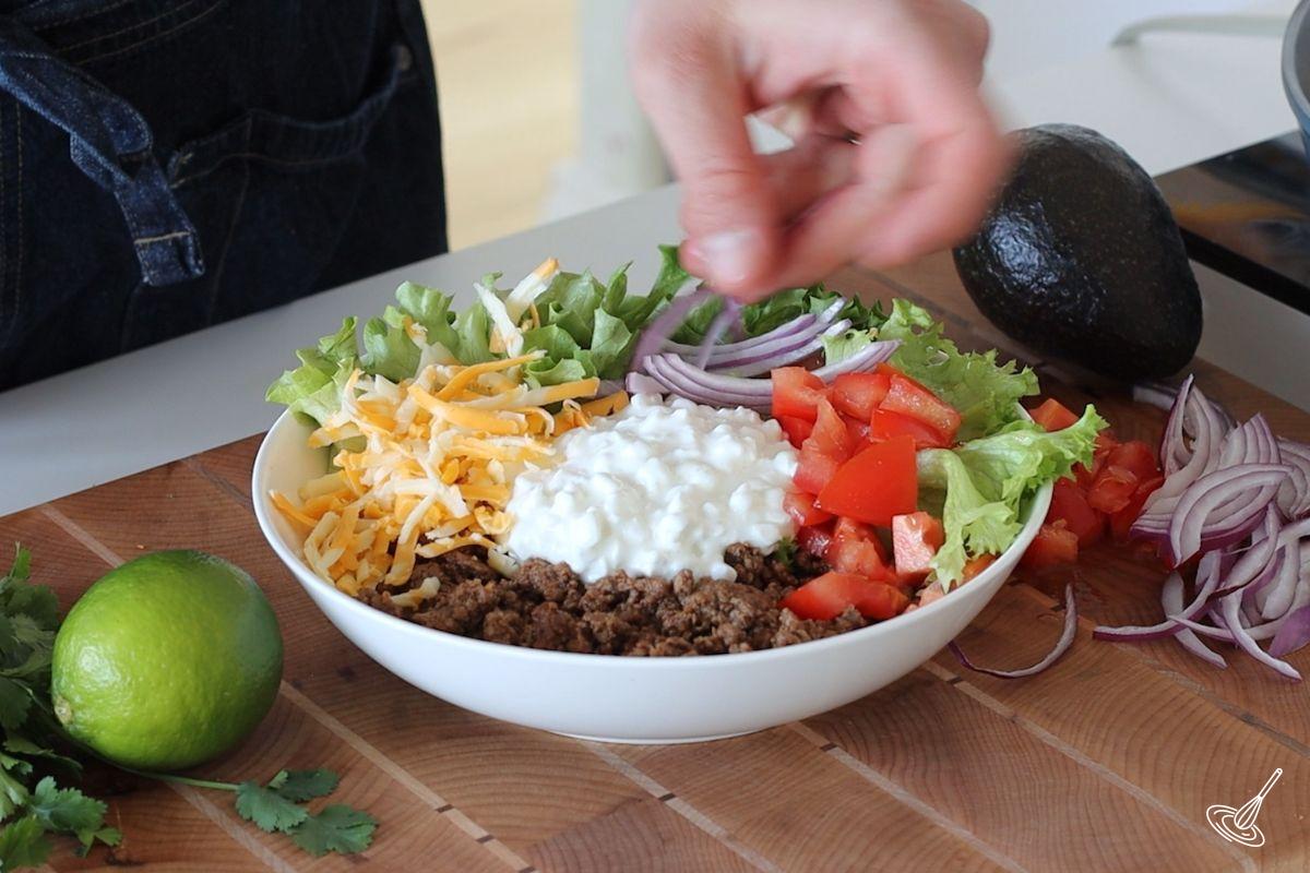 Someone garnishing a cottage cheese taco bowl with red onion. 