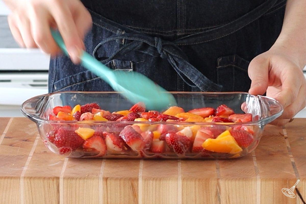 Un mélange de morceaux de fraises et de pêches dans un plat allant au four. 