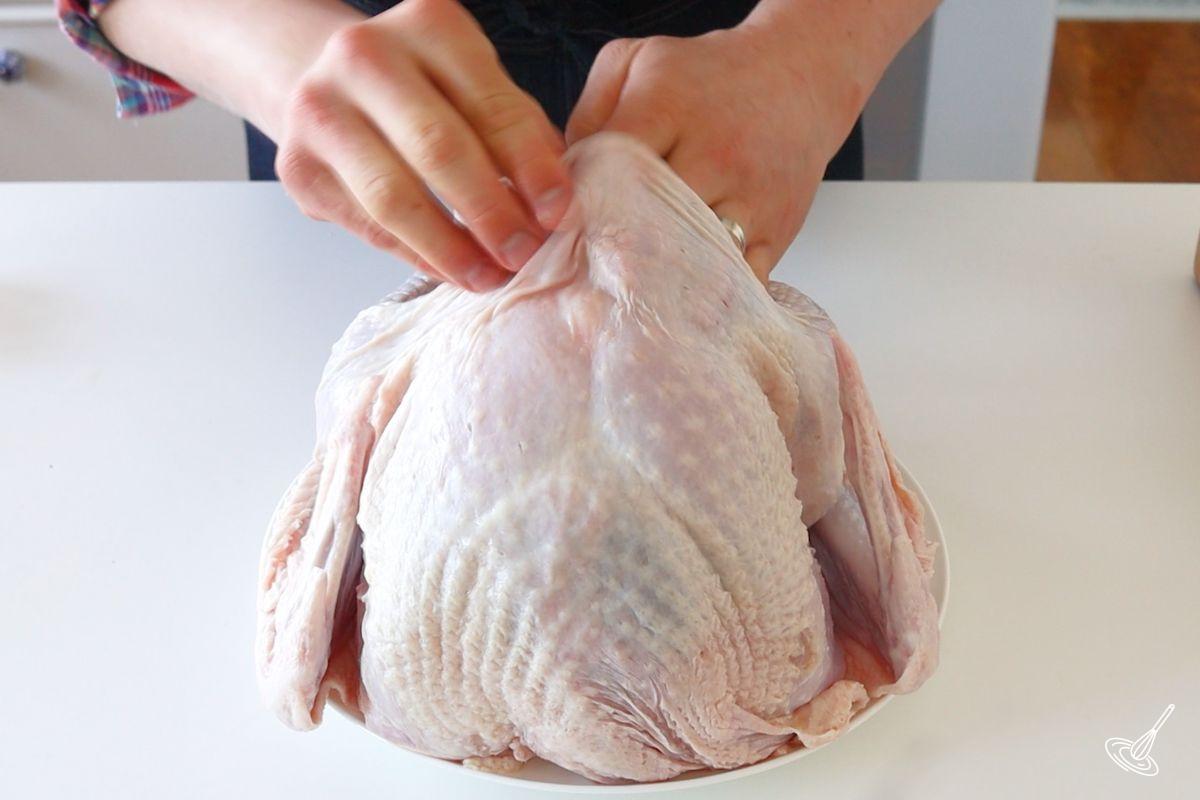 Someone using their hands to gently lift the skin off of the turkey breast.