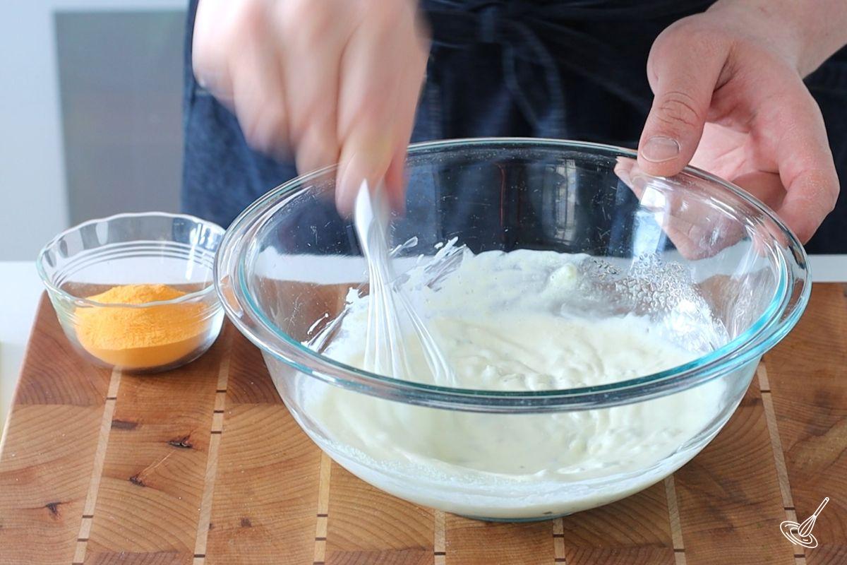 Someone whisking a mayonnaise mixture in a large bowl.