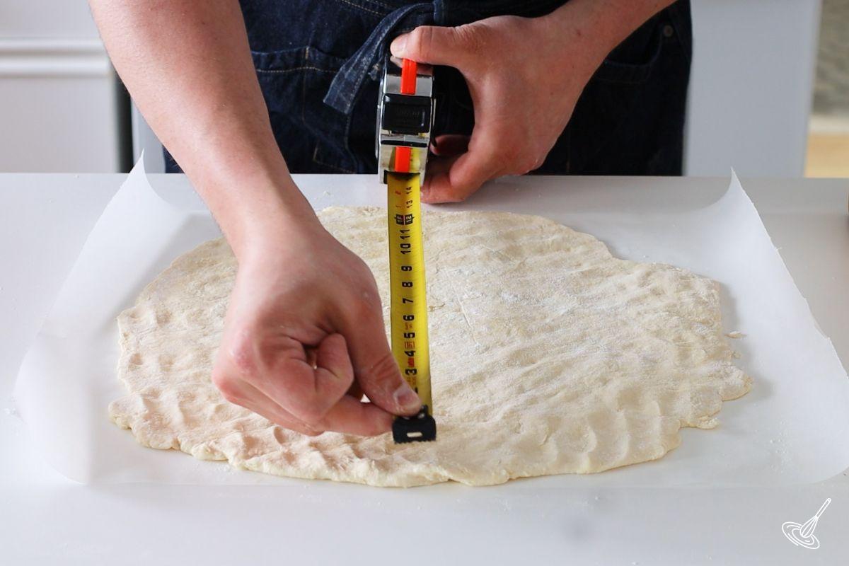 Someone using a measuring tape to measure a rolled out galette.