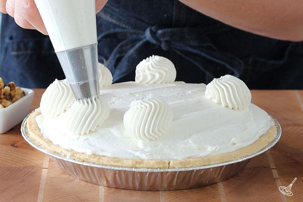 Someone piping rosettes oven a banana split pie. 