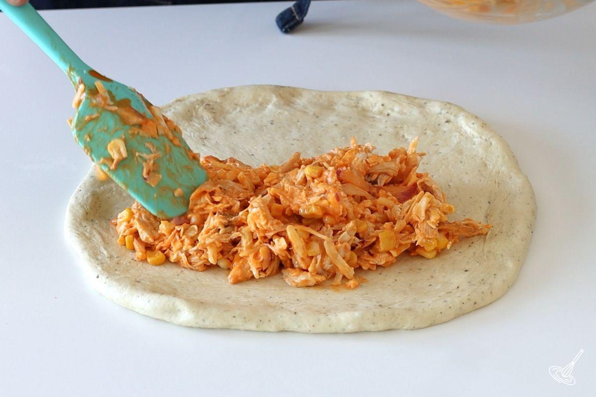 Someone adding buffalo turkey filling to a pizza dough.