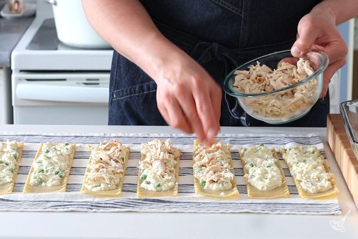 Someone placing shredded cooked turkey on top of ricotta filling on lasagna noodles.