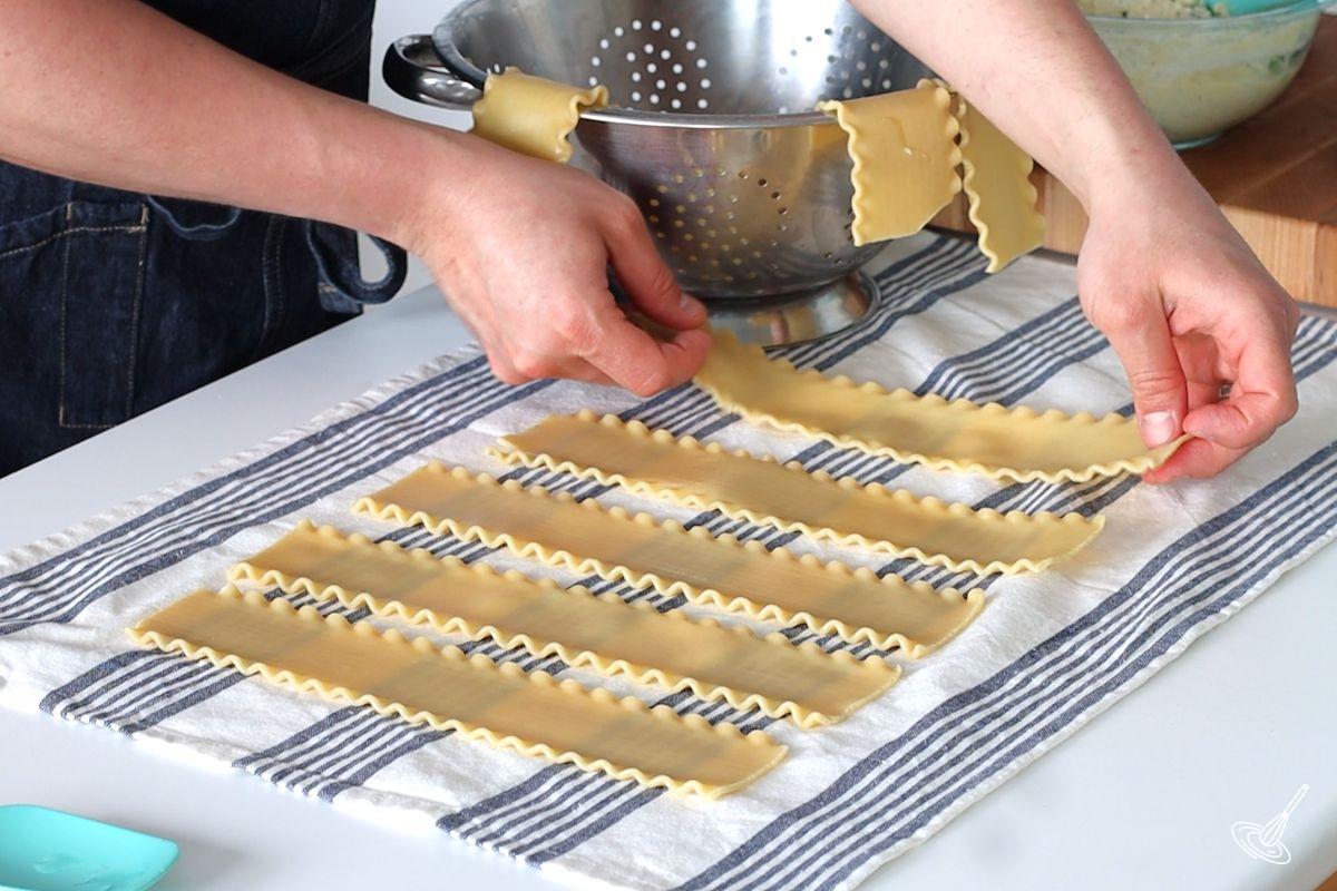 Someone laying down blanched lasagna noodles on a tea towel.