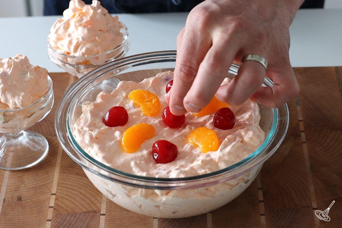 Someone decorating the Orange Jello Cottage Cheese Salad with fruit.