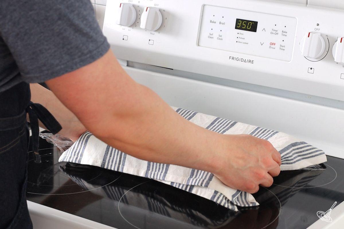 Someone placing a covered dish on top of an oven range.