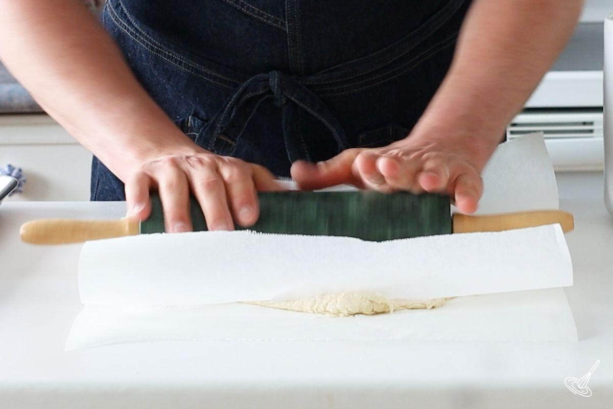Someone rolling out a galette dough between two pieces of parchments paper.