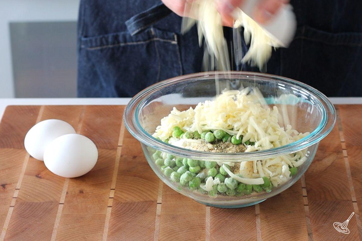Someone adding grated mozzarella to a bowl of ricotta cheese and spices.