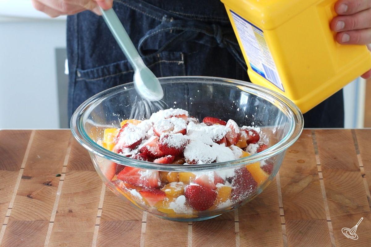 Quelqu'un saupoudre de fécule de maïs un bol de morceaux de fraises et de pêches.