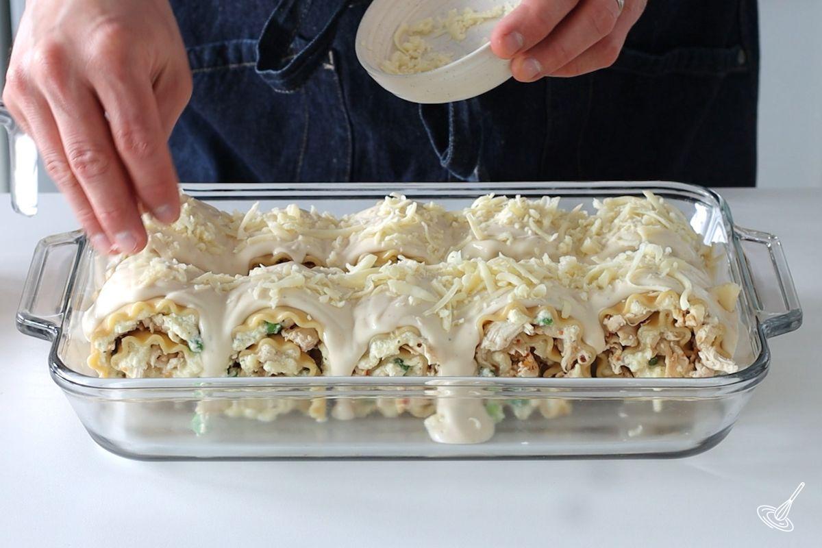 Someone sprinkling cheese and alfredo sauce on Turkey Alfredo Lasagna Rollups.