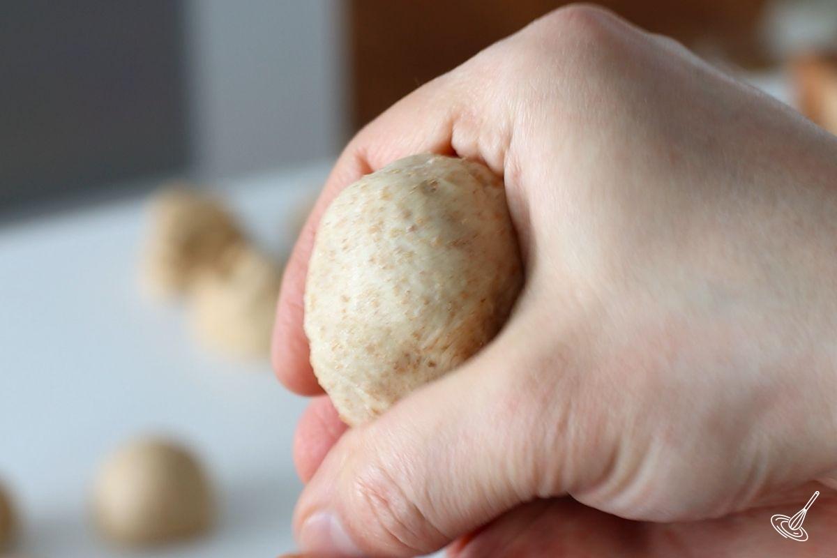 Someone using their hand to shape a round ball of dough. 