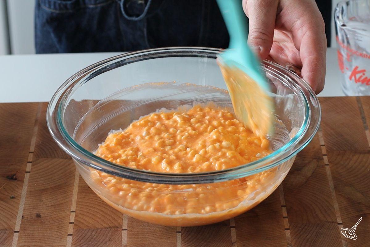 Someone stirring cottage cheese and orange jello in a bowl.
