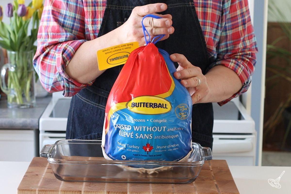 Someone placing a whole turkey in its packaging in a baking tray. 