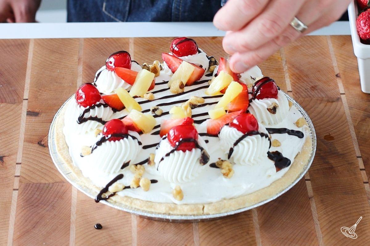 Someone decorating a Banana Split Pie with walnut pieces.