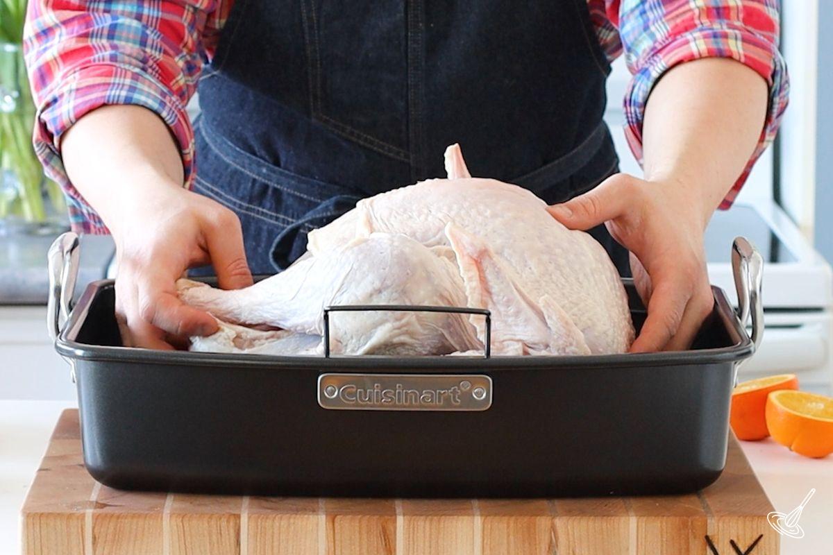 Someone placing a whole turkey in  a roasting pan. 