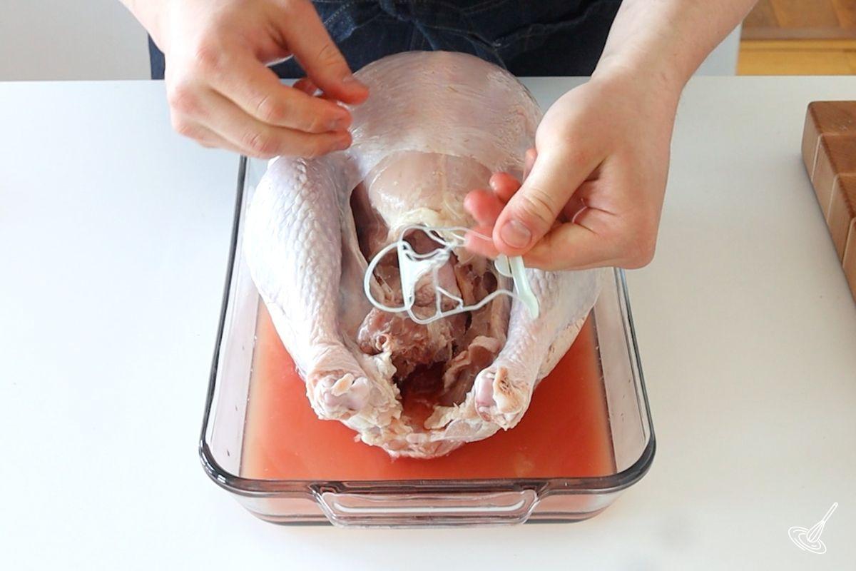 Someone removing a plastic tie from a raw turkey roast.