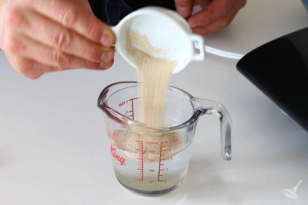 Someone adding instant dry yeast to a measuring cup of warm water and honey.