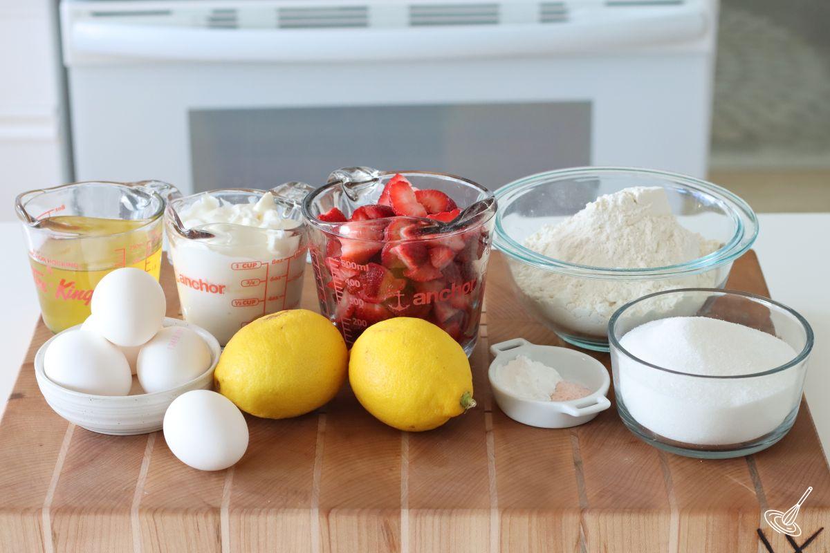 Ingredients on a cutting board including strawberries, lemons, flour, eggs, and sugar.
