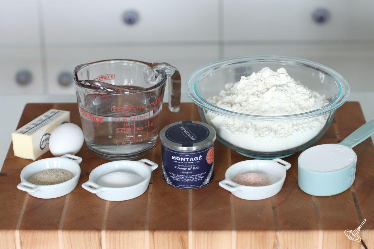 Ingredients on a cutting board including flour, salt, water, yeast, and sugar.