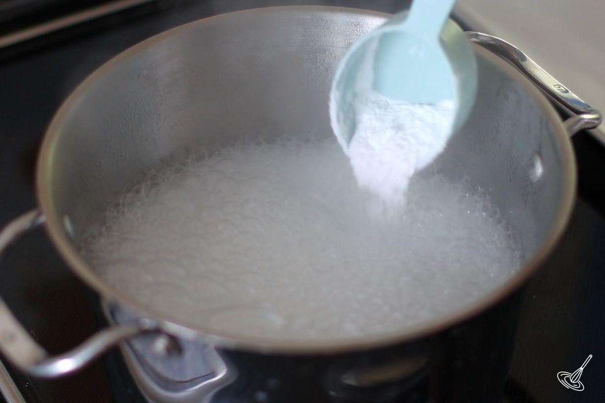 Someone adding baking soda to a large pot of simmering water.