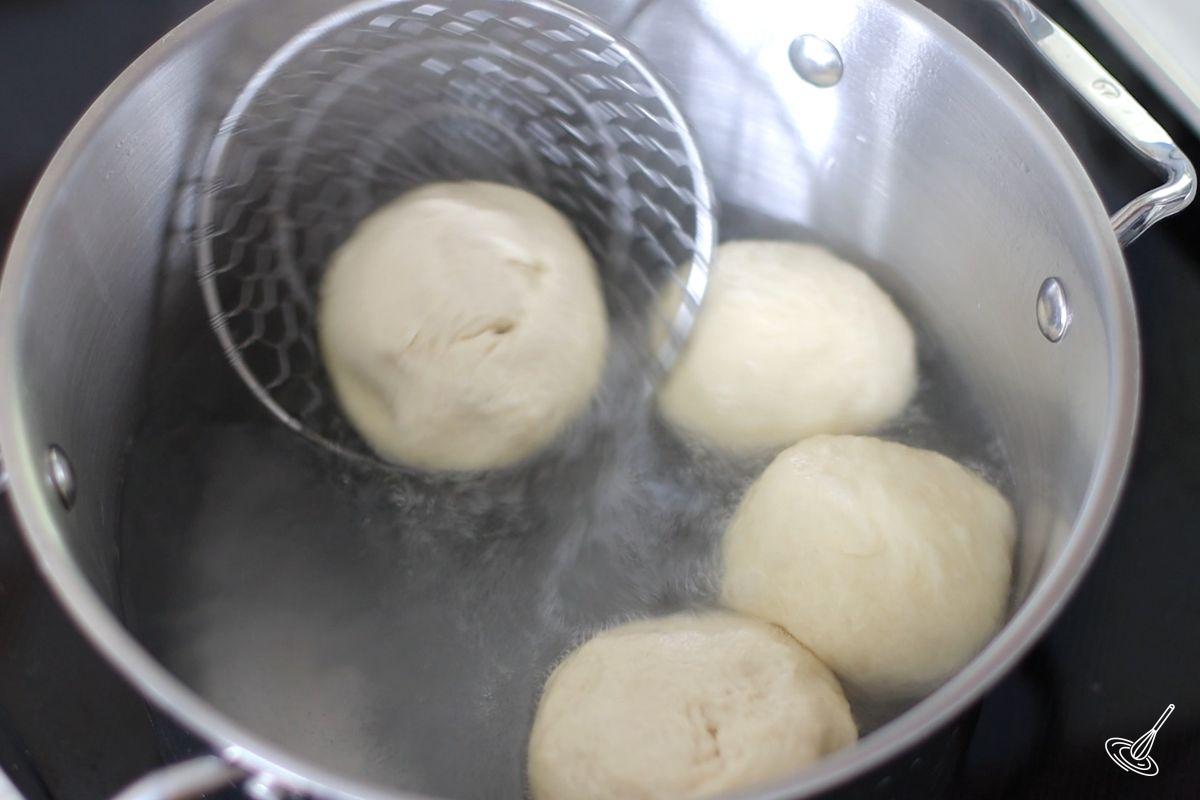 Someone flipping over a ball of dough in a pot of simmering water.