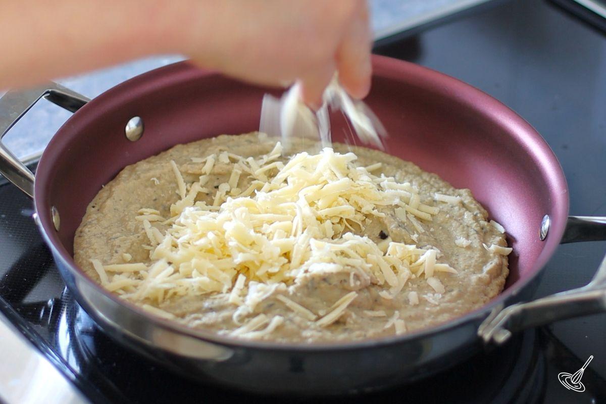 Someone adding grated cheese to a pan of aubergine cream pasta sauce. 