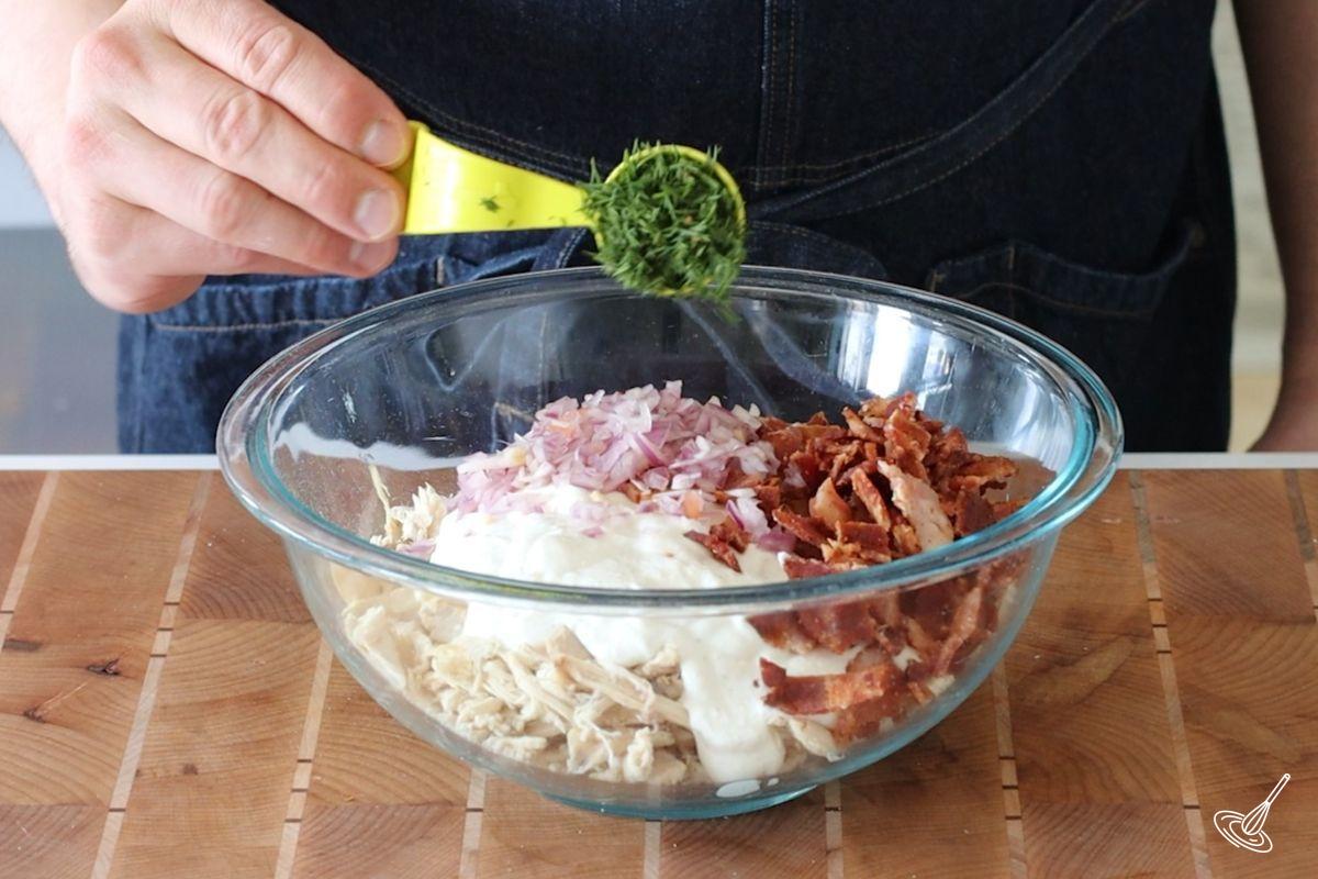 Someone adding chopped dill to a large bowl of shredded chicken. 