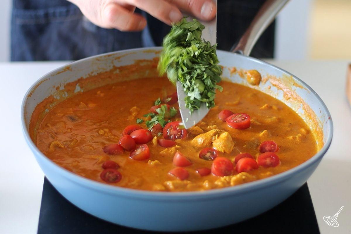 Someone adding chopped fresh cilantro to a skillet of chicken curry with buttermilk. 