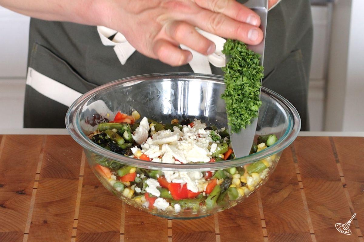 Someone adding chopped parsley to a bowl of Roasted Corn and Asparagus salad. 