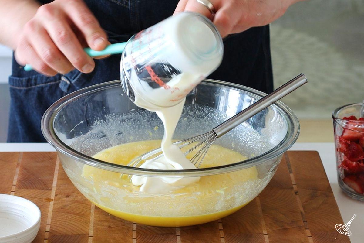 Someone adding sour cream to a large bowl of egg mixture.