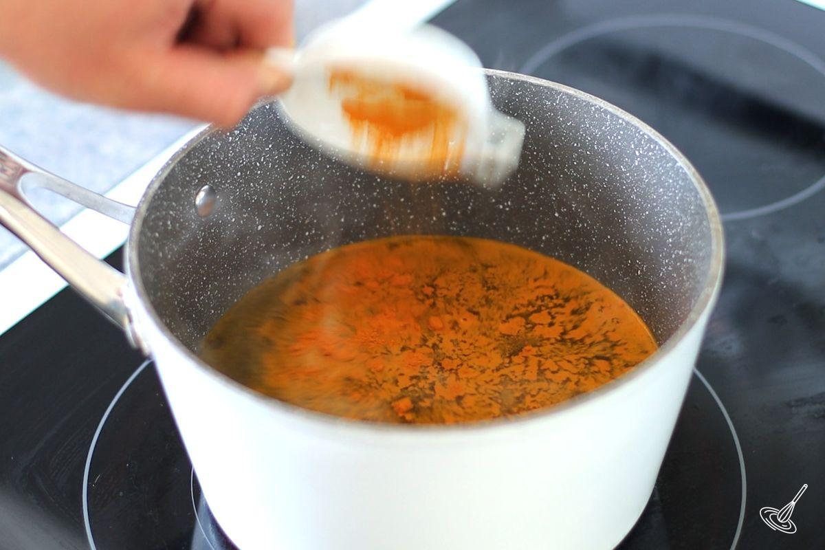 Someone adding turmeric powder to a pot of simmeing water.
