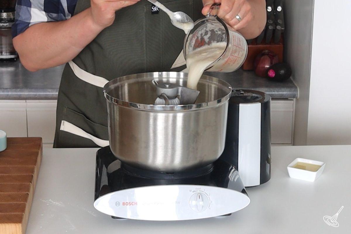 Someone adding yeast to a stand mixer.